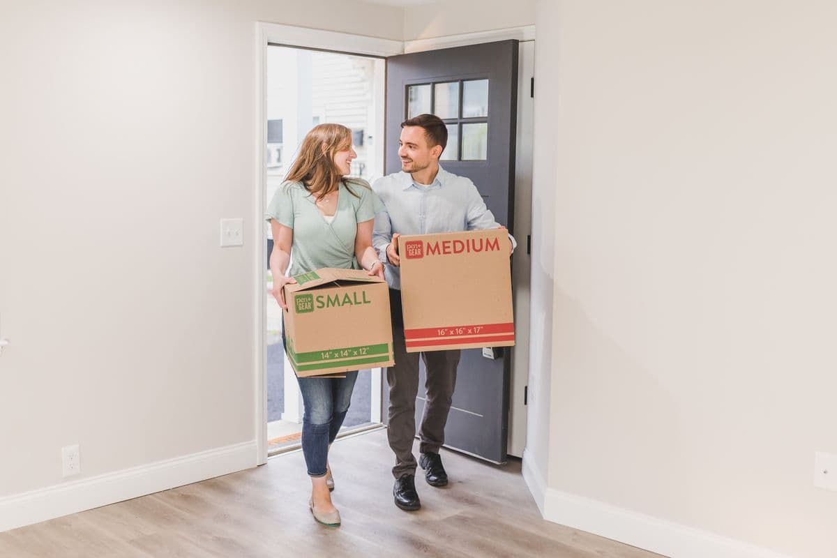 A couple carrying moving boxes into a new home
