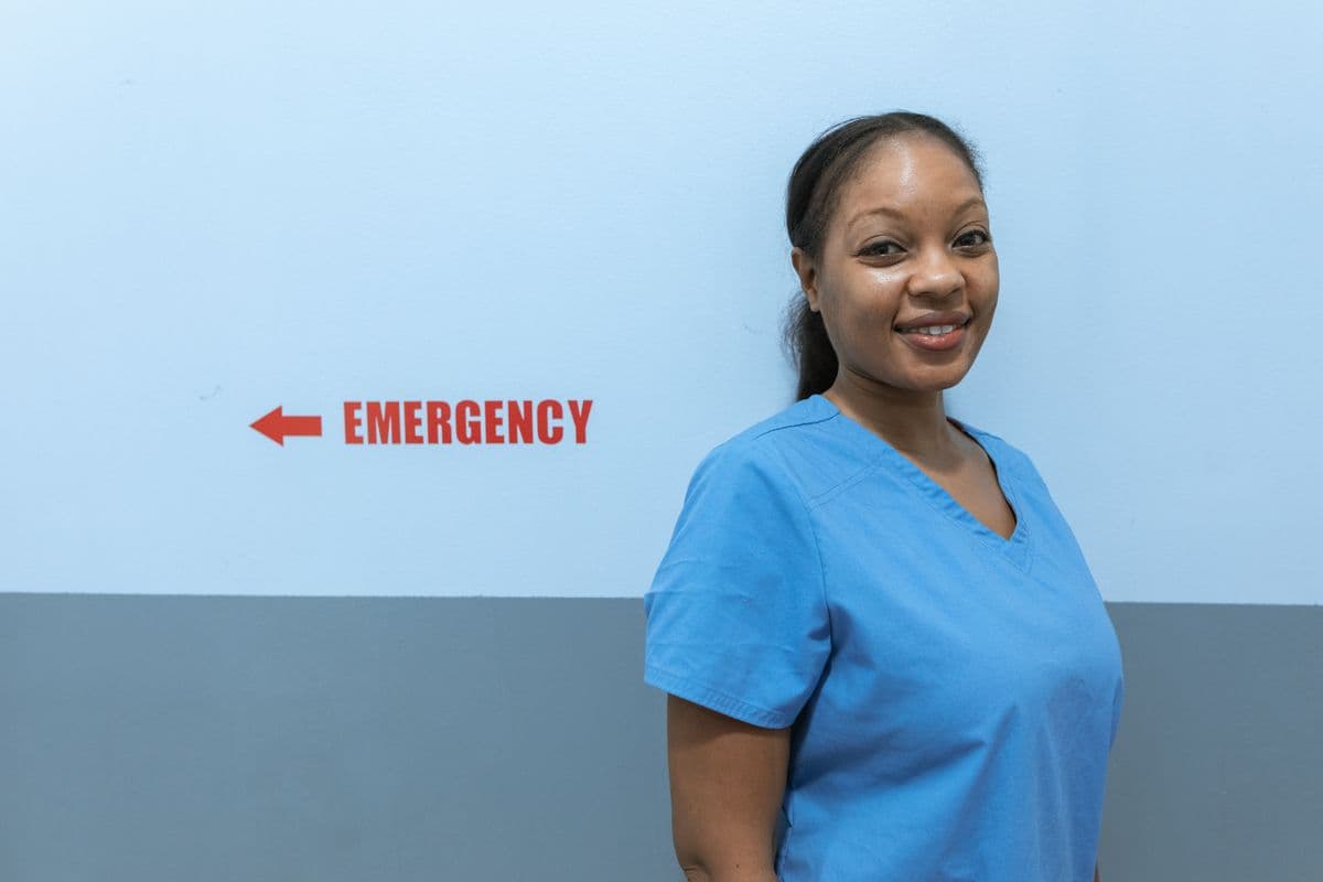 A smiling nurse in blue scrubs in a hospital hallway