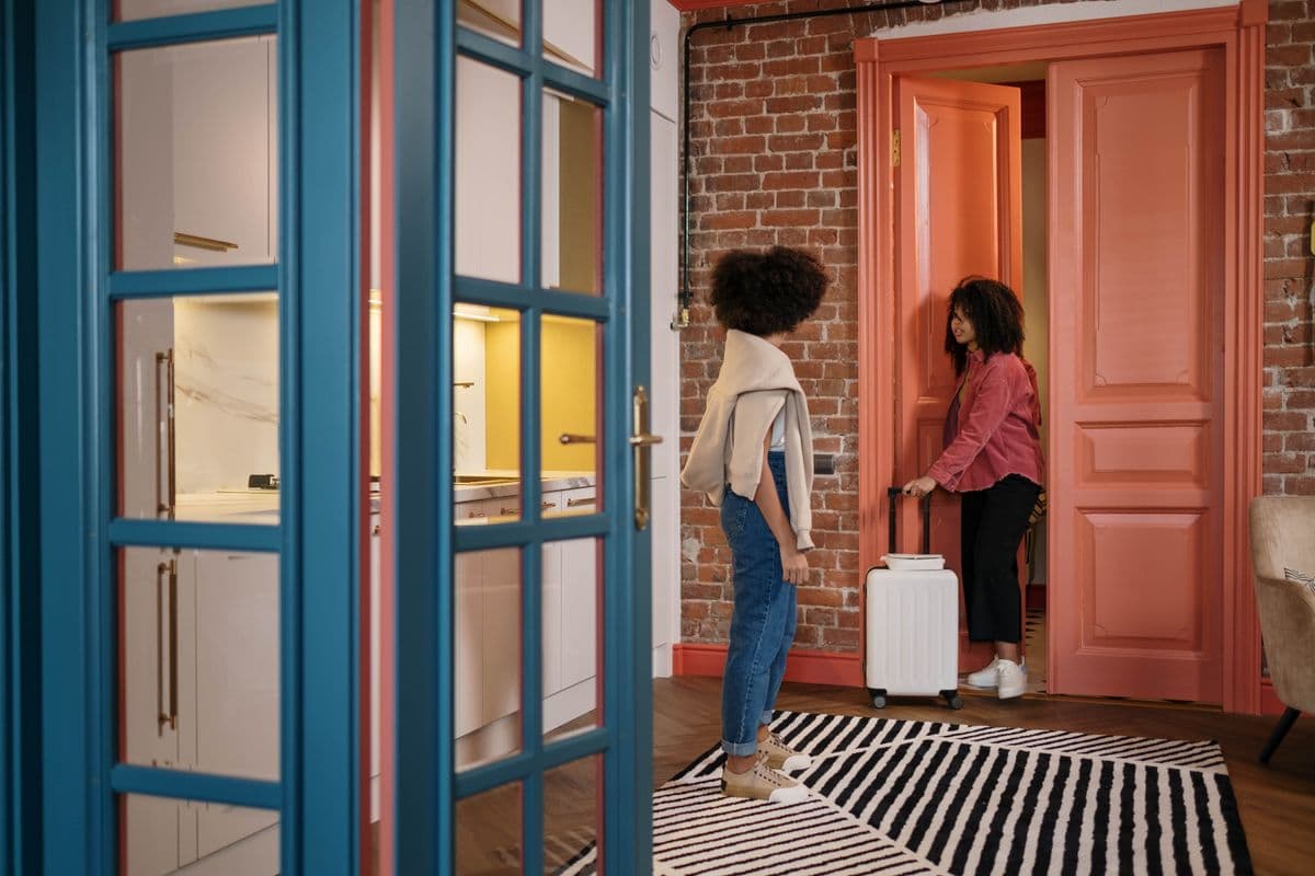 A traveler with a suitcase being welcomed at a front door