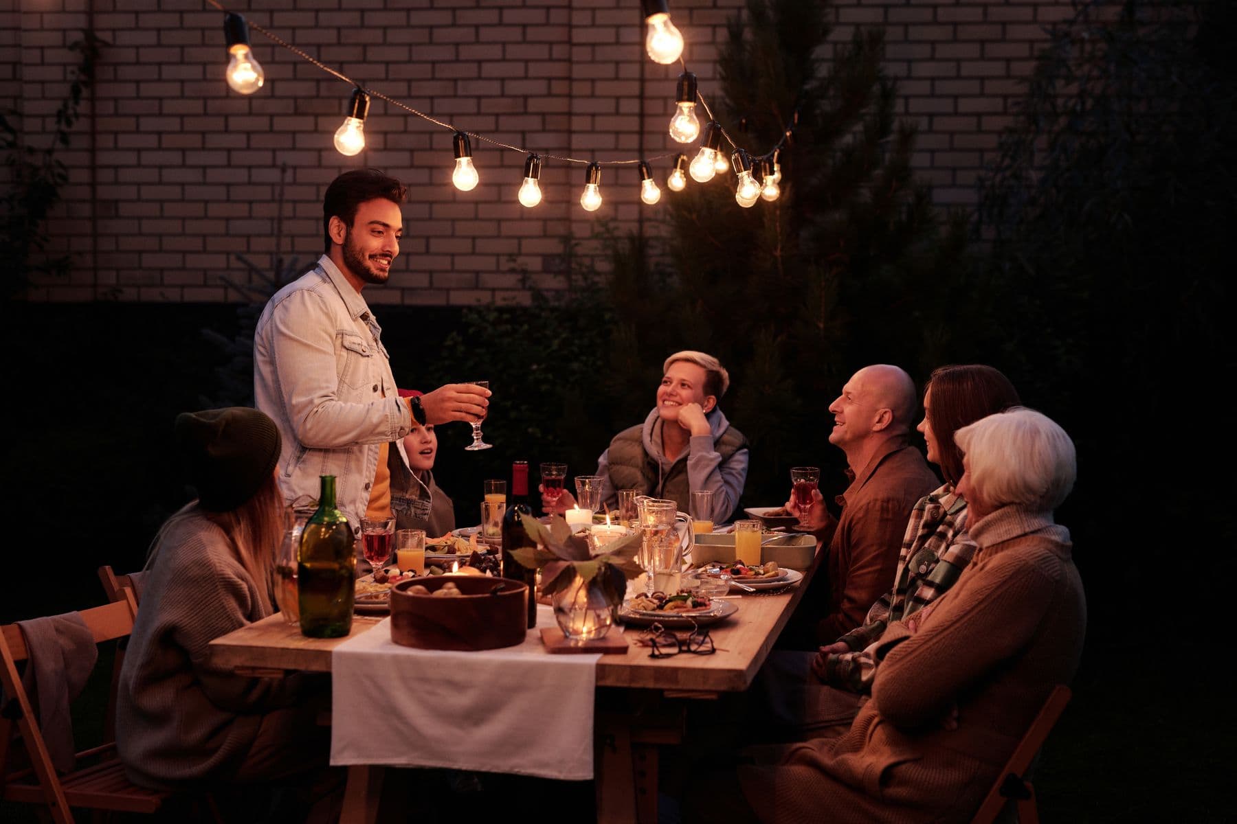 Neighbors sharing dinner outdoors under string lights