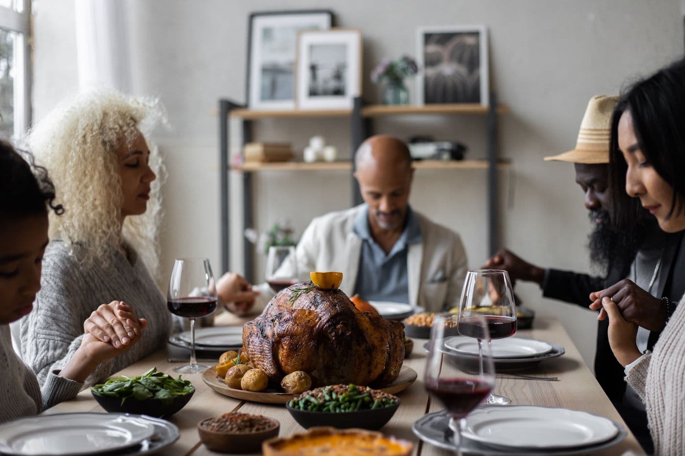Friends holding hands to pray before dinner at a home table