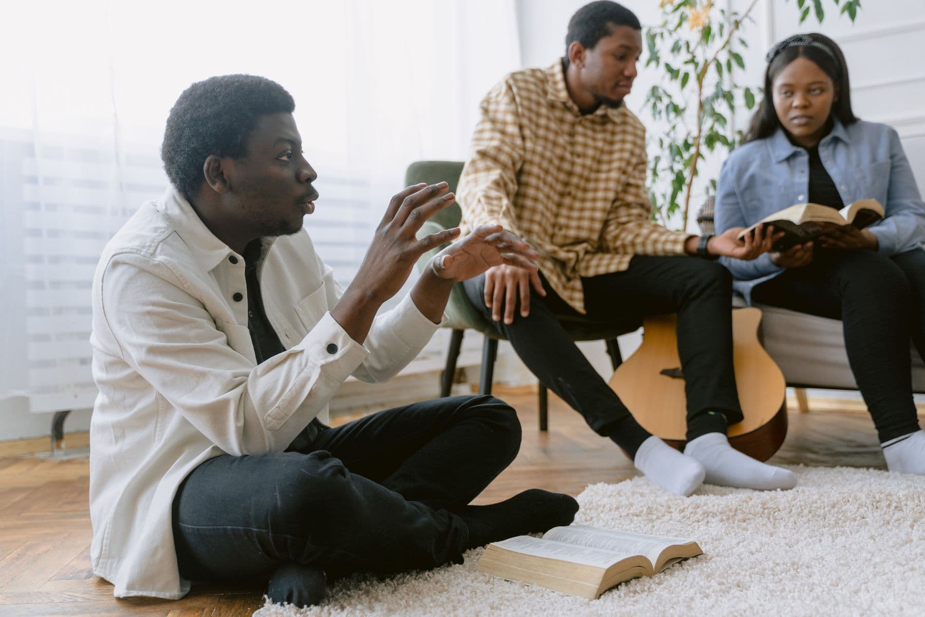 Three friends with open Bibles talking on a living-room floor