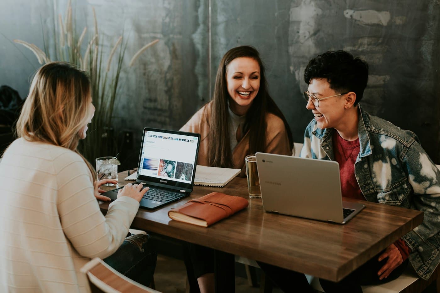 Three people laughing together over laptops at a cafe table